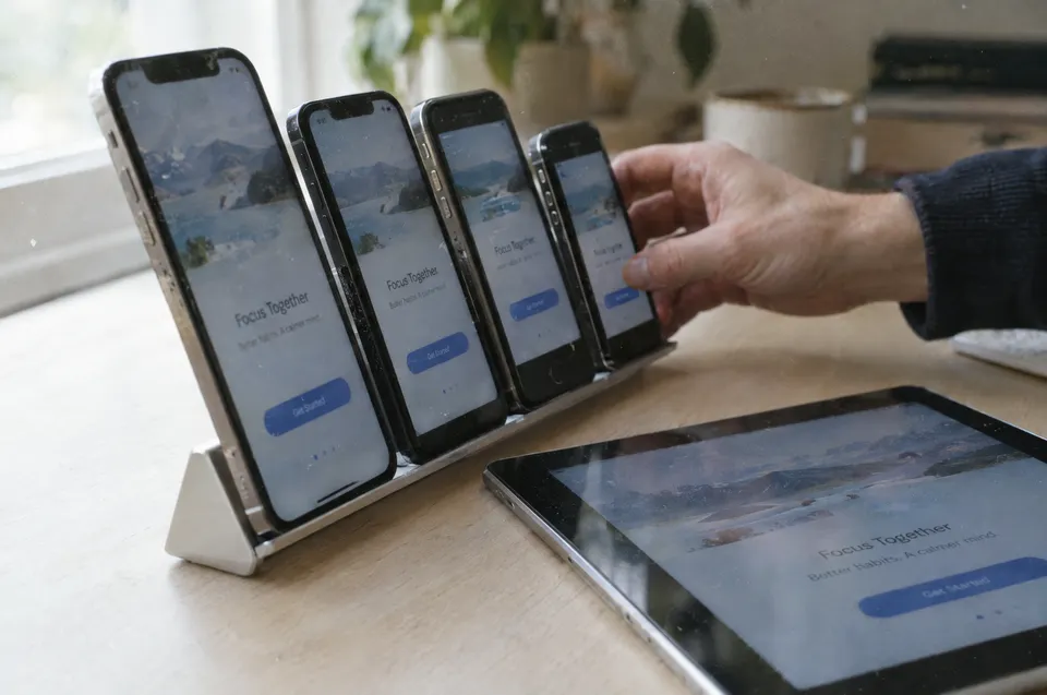 Several smartphones on a stand show the same app screen while a hand adjusts one of them.